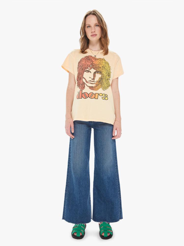 Front full body view of a woman wearing a faded orange crew neck tee featuring an oversized fit and a large "THE doors" graphic.