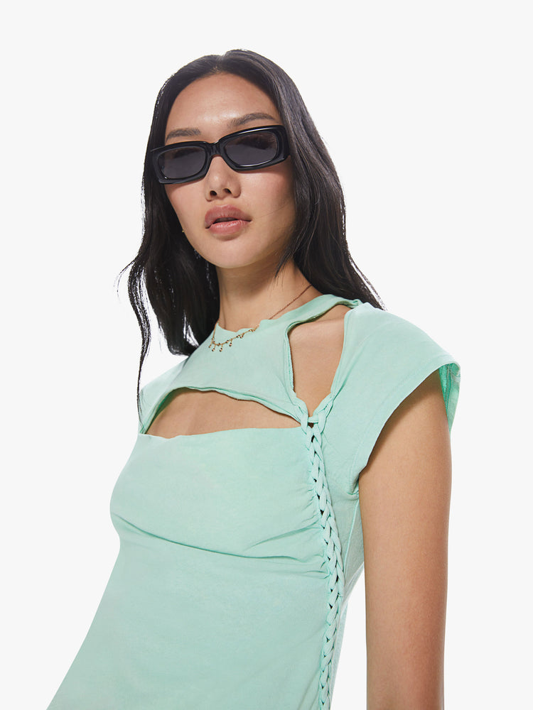 A front close up view of a Womens asymmetrical sleeve top in a mint green hue, featuring cutouts at the shoulder and chest and a braid down the left side.