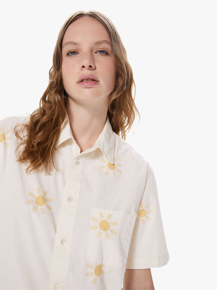 WOMEN Front close up view of a woman wearing a white, short sleeve collared shirt featuring a front pocket, a sun pattern, and a boxy oversized fit.
