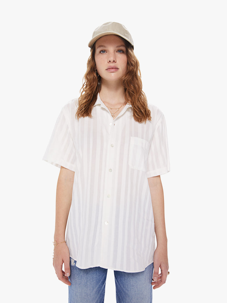 WOMEN Front view of a woman wearing a white, short sleeved collared shirt, featuring embroidered stripes, a front patch pocket, and a boxy oversized fit.