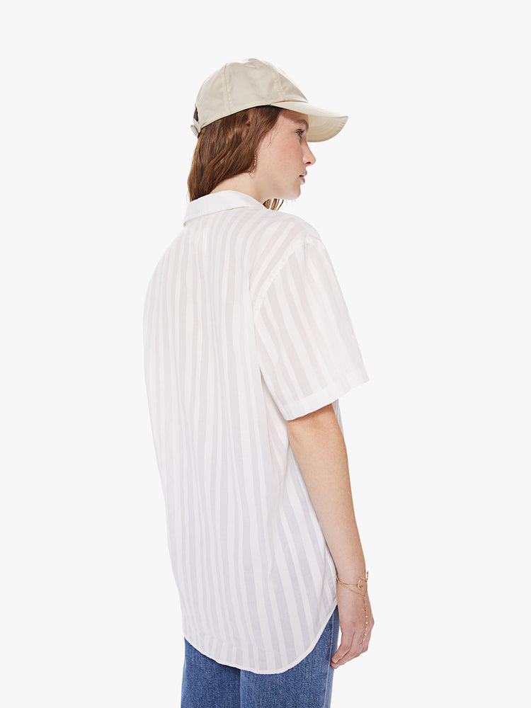 WOMEN Back view of a woman wearing a white, short sleeved collared shirt, featuring embroidered stripes, a front patch pocket, and a boxy oversized fit.