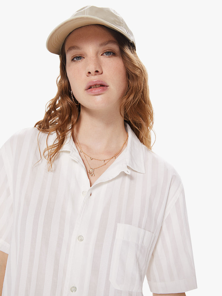 WOMEN Front close up view of a woman wearing a white, short sleeved collared shirt, featuring embroidered stripes, a front patch pocket, and a boxy oversized fit.