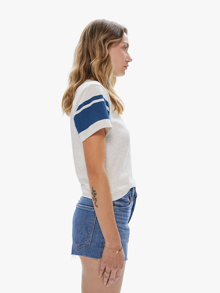 Side view of a woman wearing an oatmeal pocket crew neck featuring two navy stripes on the sleeves.