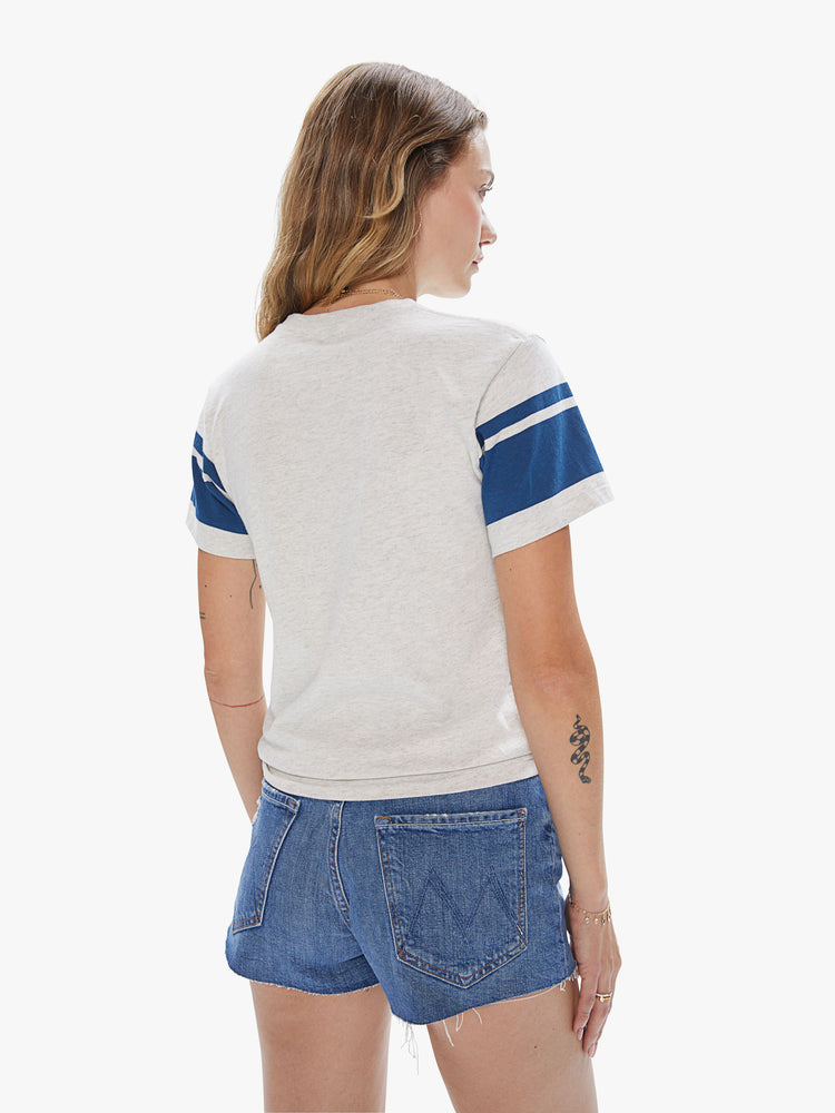 Back view of a woman wearing an oatmeal pocket crew neck featuring two navy stripes on the sleeves.