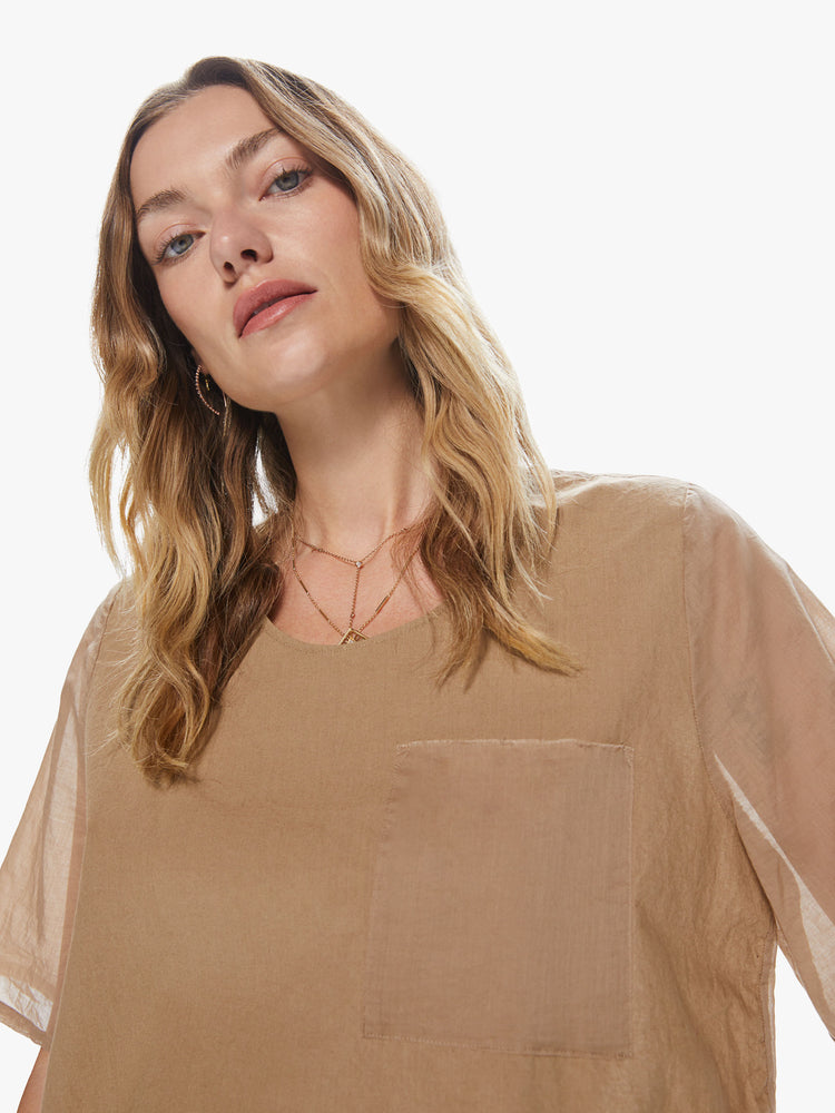 Front close up view of a woman wearing a khaki crew neck top featuring a chest pocket and sheer sleeves.