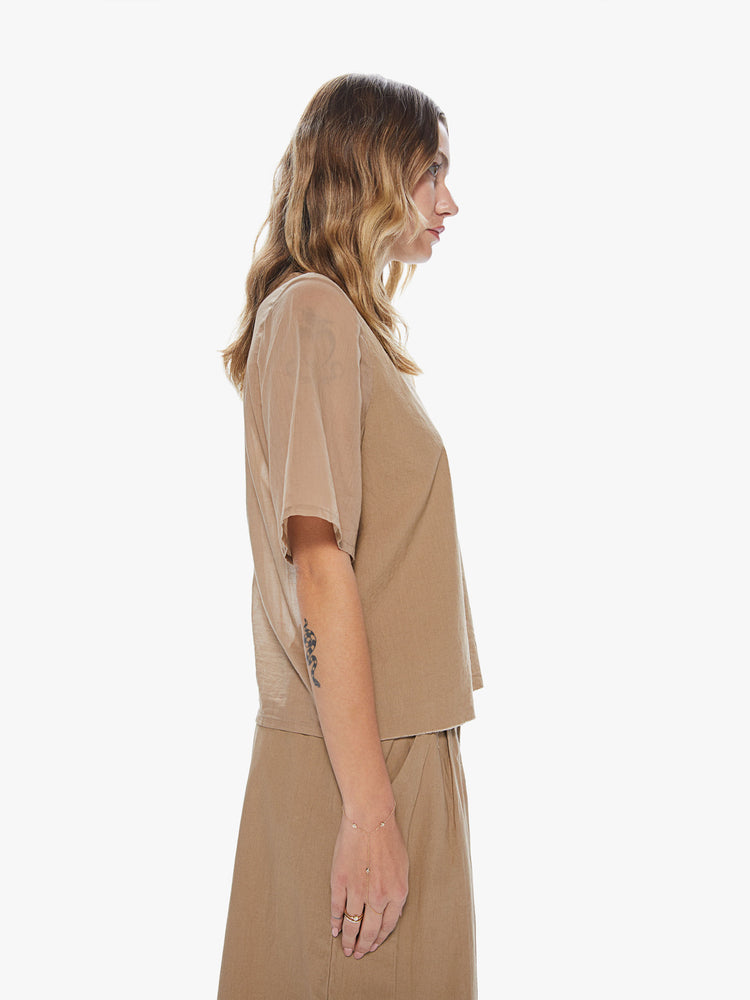 Side view of a woman wearing a khaki crew neck top featuring a chest pocket and sheer sleeves.