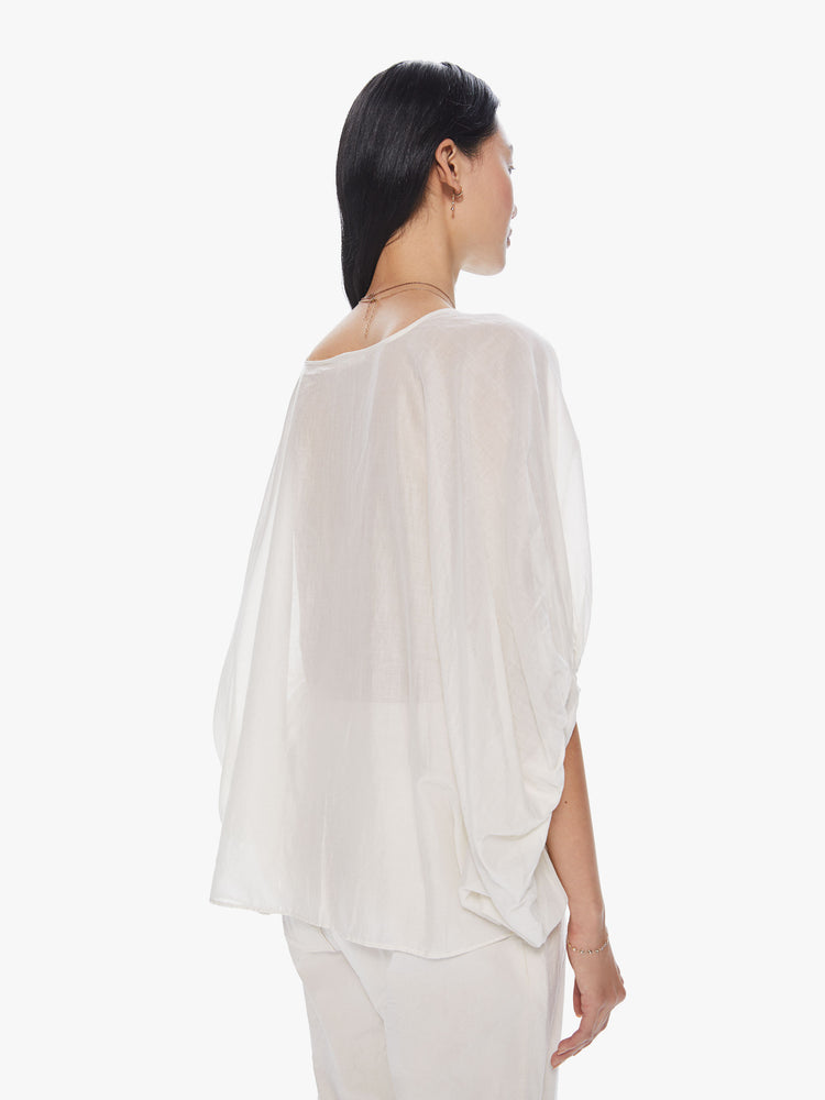 Back view of a woman wearing a sheer, off white top with elbow length balloon sleeves and a loose fit.