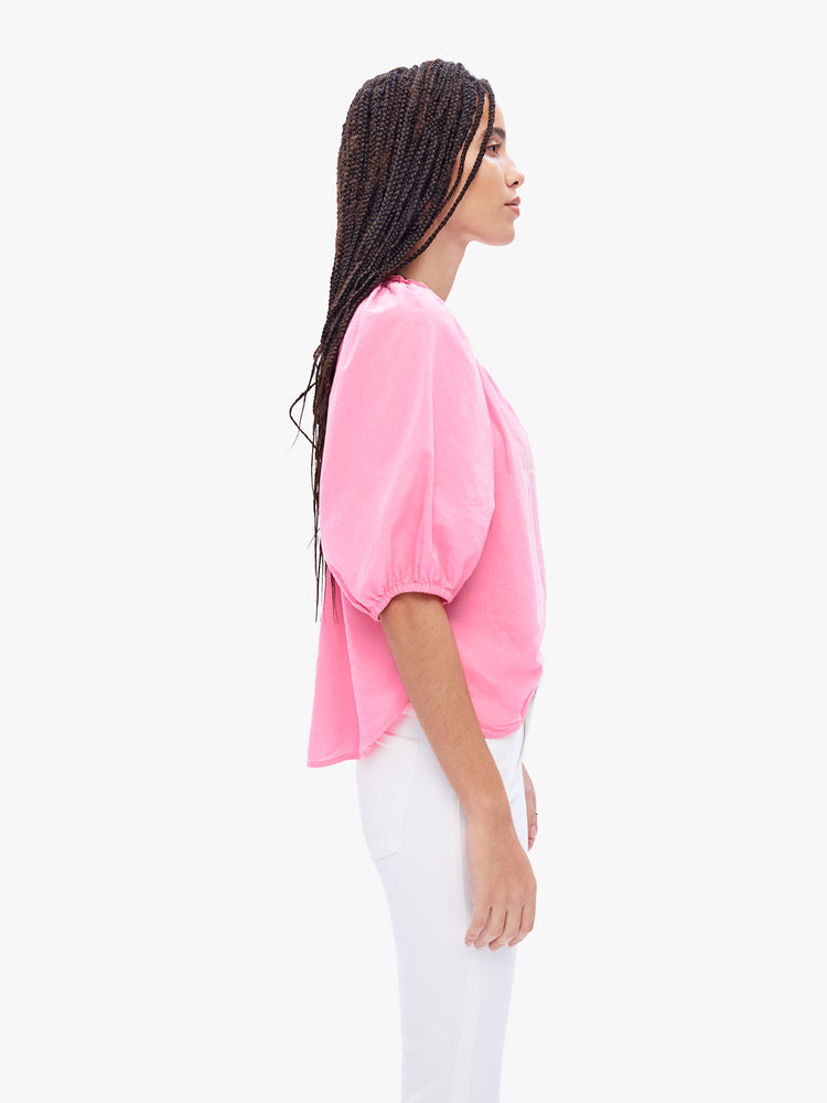 Side view of a woman in effortless top from XiRENA, made from 100% cotton in a baby pink hue, the blouse features a ruffled collar with a deep Vneck, elbow-length balloon sleeves and a loose fit