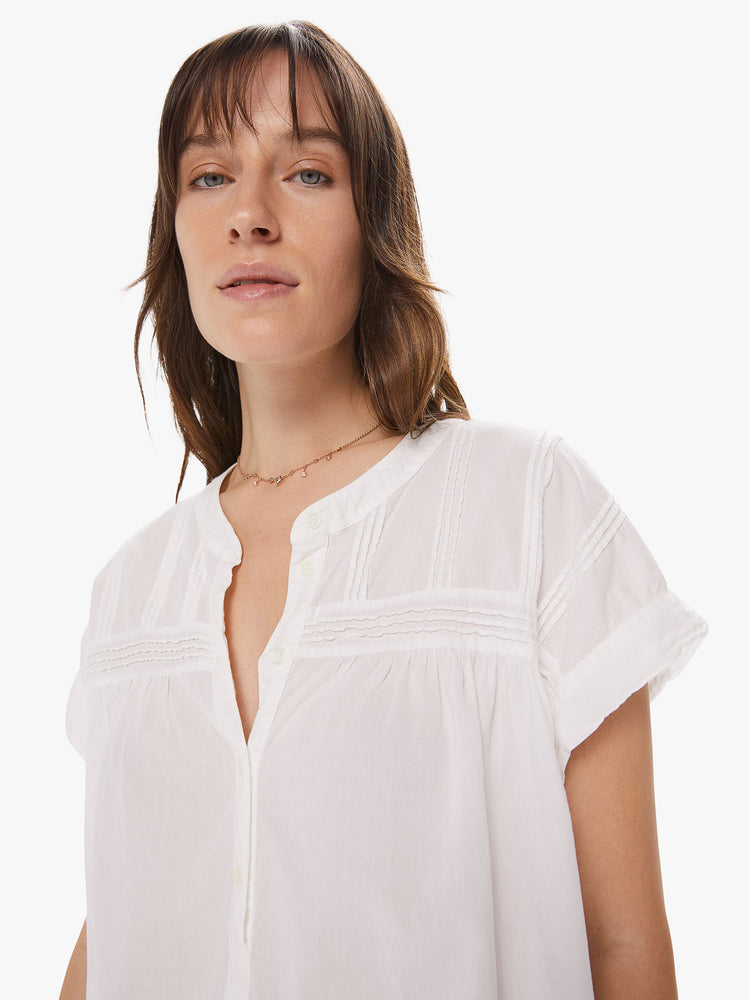 Front close up view of a woman wearing a white top featuring embroidered details at the chest and a boxy fit.