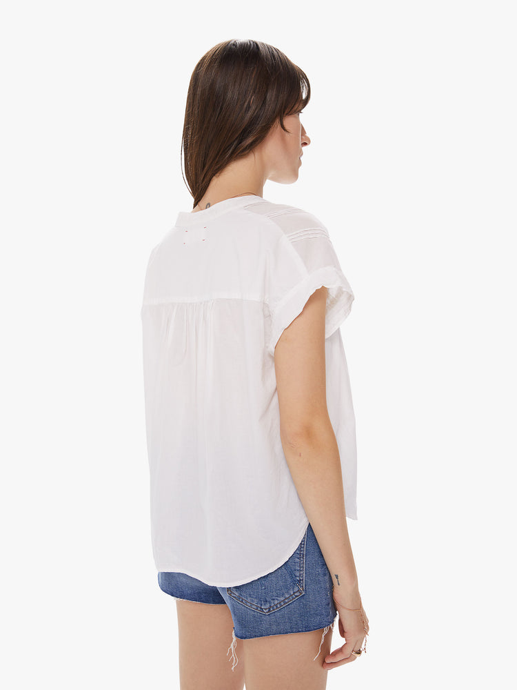 Back view of a woman wearing a white top featuring embroidered details at the chest and a boxy fit.
