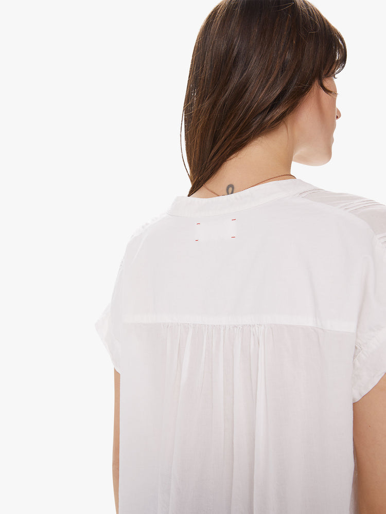 Back detail view of a woman wearing a white top featuring embroidered details at the chest and a boxy fit.