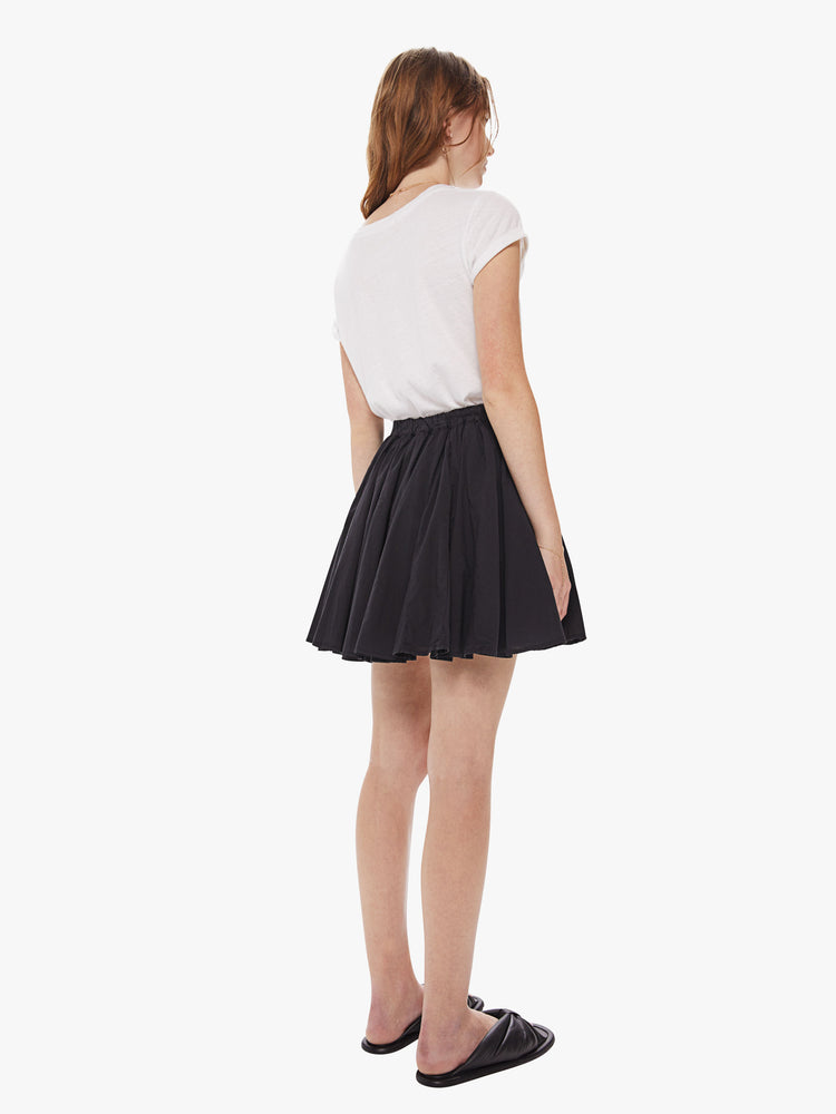Back view of a woman wearing a black skirt, featuring a high elastic wiast and a short hem.