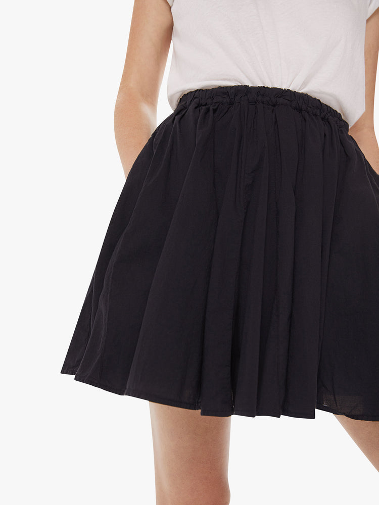 Front close up view of a woman wearing a black skirt, featuring a high elastic wiast and a short hem.