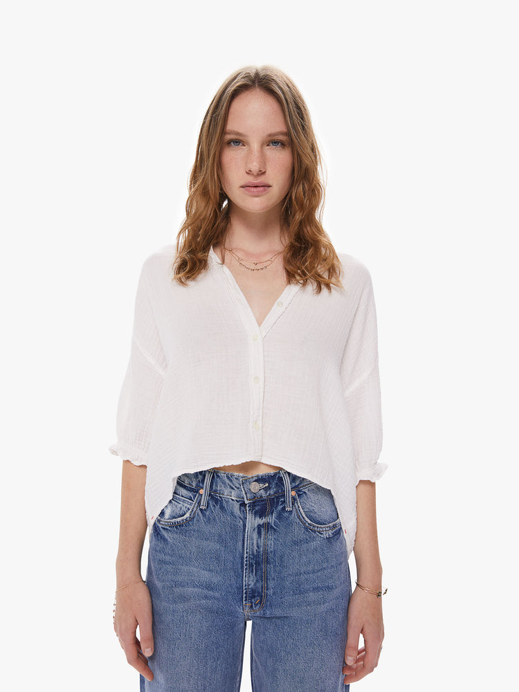 Front view of  a woman wearing a white button down top featuring a deep v and a cropped hem.