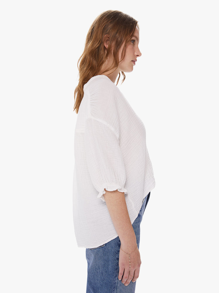 Side view of  a woman wearing a white button down top featuring a deep v and a cropped front hem.