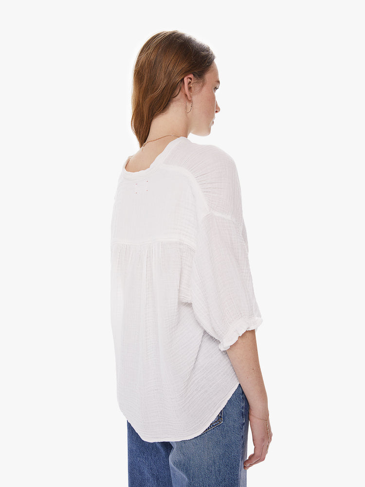 Back view of  a woman wearing a white button down top featuring a deep v and a long back hem.