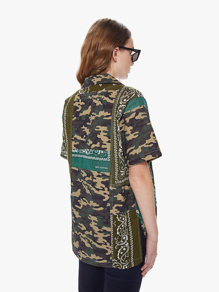 Back view of a woman wearing an oversized short sleeve button down shirt featuring multiple green camo and bandana prints.