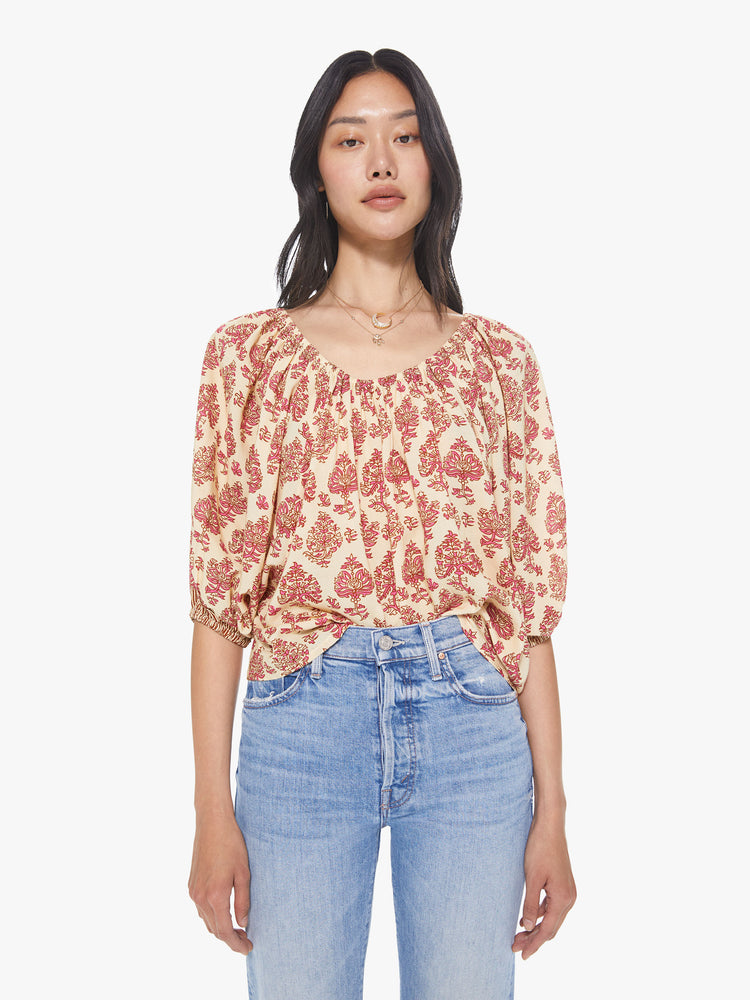Front view of a women's light beige scoop-neck blouse with all-over red floral print and short sleeves