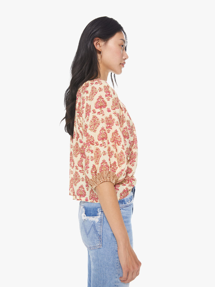 Side view of a women's light beige scoop-neck blouse with all-over red floral print and short sleeves