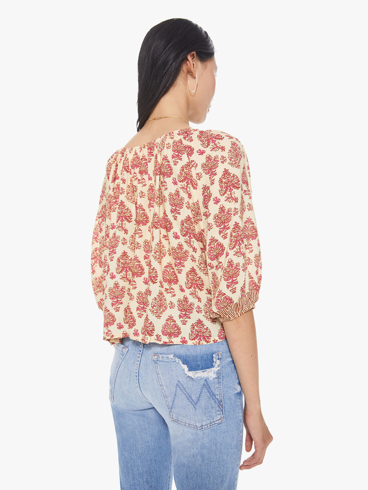 Back view of a women's light beige scoop-neck blouse with all-over red floral print and short sleeves