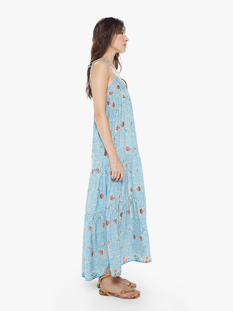 Side view of a women's light blue tiered maxi dress with all-over floral print and spaghetti straps