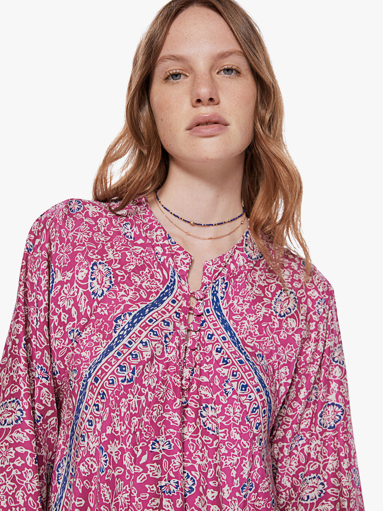 Front close up view of a woman wearing a pink maxi dress featuring a blue floral print, a buttoned v-neck and long sleeves.