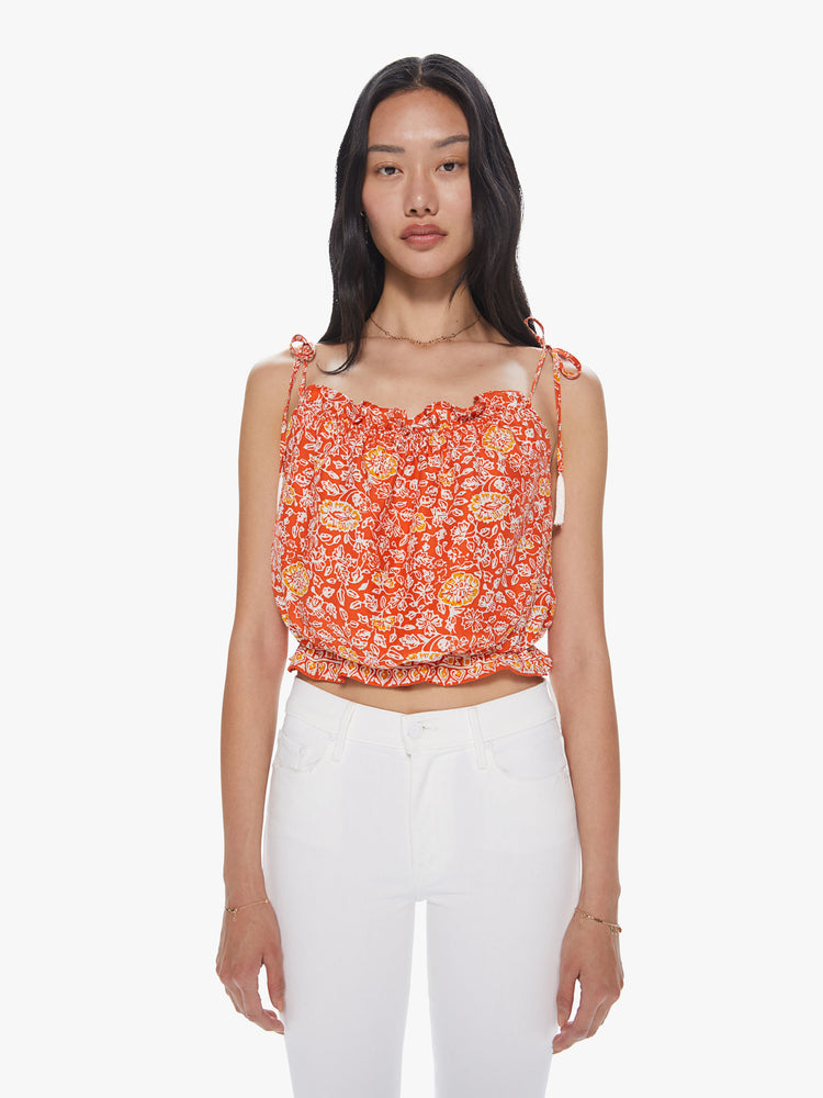Front view of a woman wearing a bright orange top featuring a yellow and white floral print, thin tie straps, and a cropped elastic body.