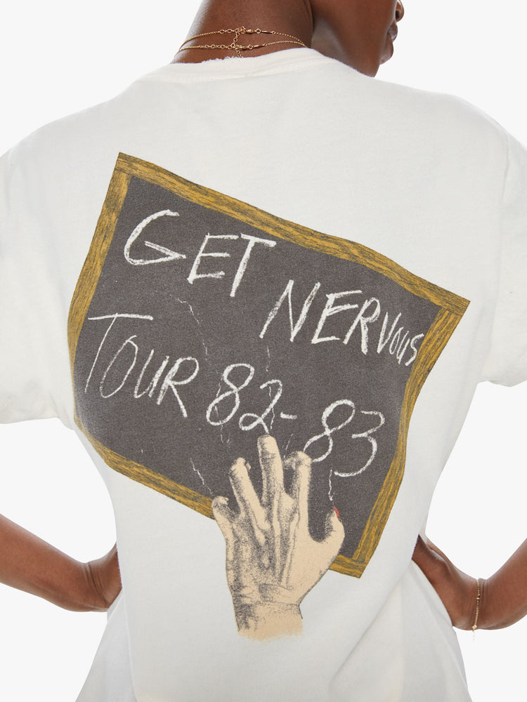 Back close up view of a woman wearing an off white crew neck tee featuring a vintage band inspired concert graphic on the back reading "GET NERVOUS TOUR 82-83" with distressed details.-
