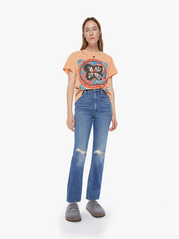 Front full body view of a woman wearing a peach colored crew neck tee featuring a vintage concert inspired KISS band graphic reading "ROCK AND ROLL OVER" and distressed details. 