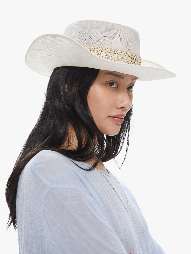 Side view of a woman wearing a white linen hat featuring a western inspired shape and leather lace trim.