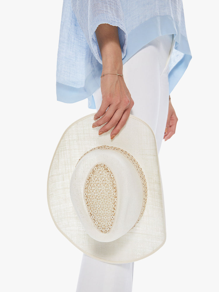 Side view of a woman holding a white linen hat featuring a western inspired shape and leather lace trim.