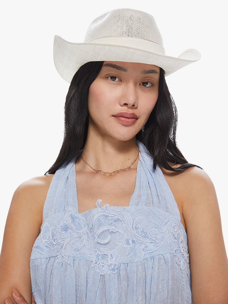 Front view of a woman wearing a white linen hat featuring a western inspired shape and leather trim.