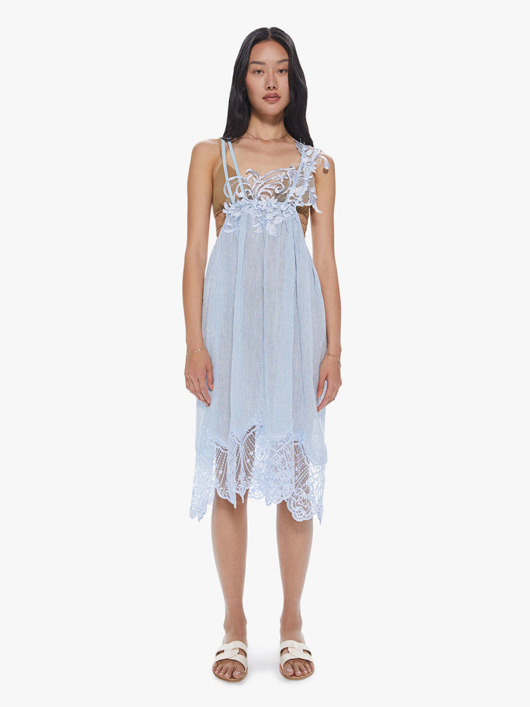 Front view of a woman wearing a sheer light blue linen dress with thin straps and lace trim detailing.