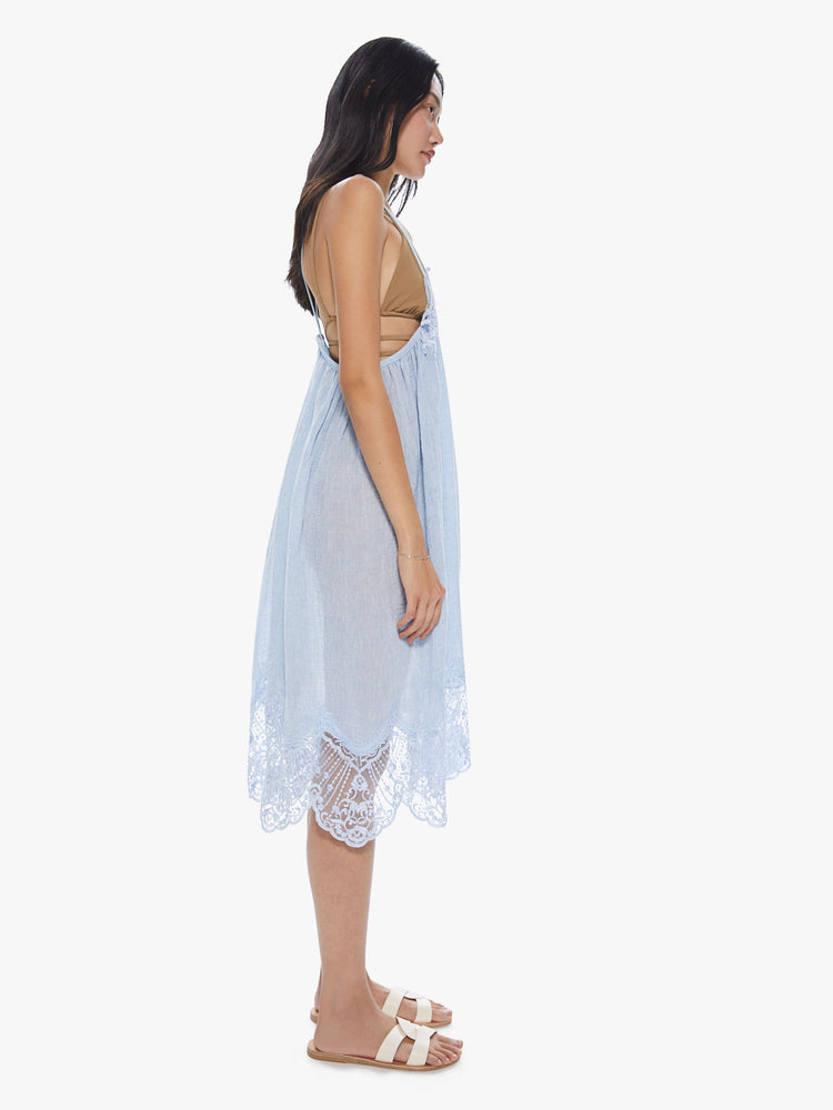 Side view of a woman wearing a sheer light blue linen dress with thin straps and lace trim detailing.