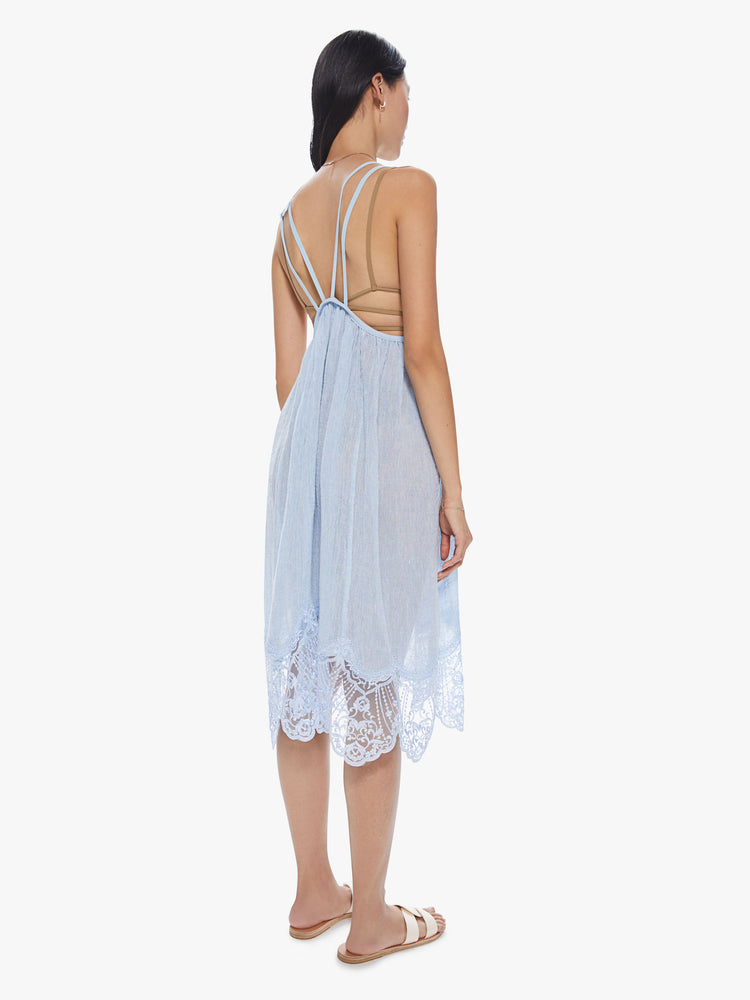 Back view of a woman wearing a sheer light blue linen dress with thin straps and lace trim detailing.