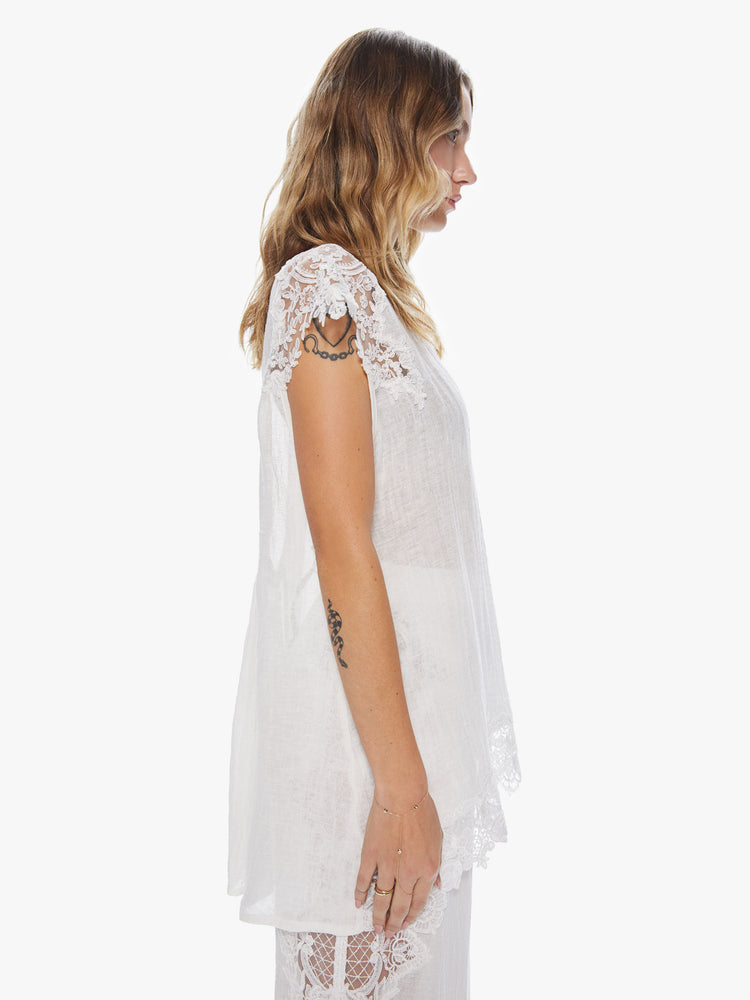 Side view of a woman wearing a white blouse with sheer lace sleeves and bottom hem.