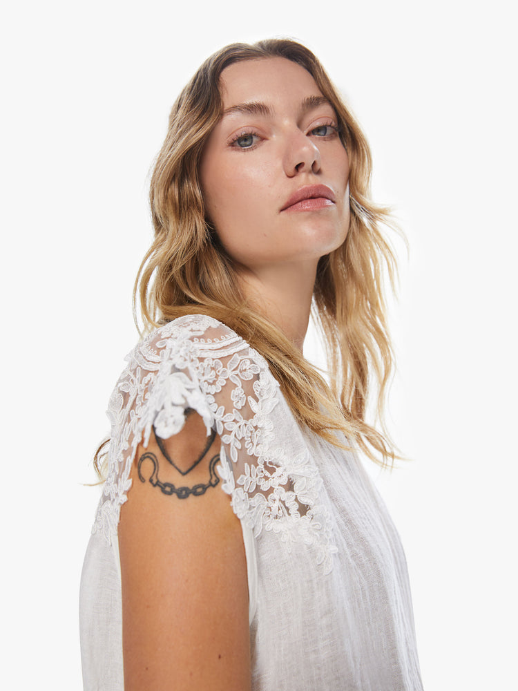 Side close up view of a woman wearing a white blouse with sheer lace sleeves and bottom hem.