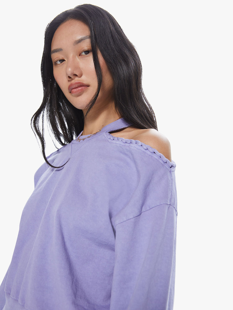 Front close up view of a woman wearing a cropped lavender pullover featuring dropped sleeves and cut-out shoulders with braided details.