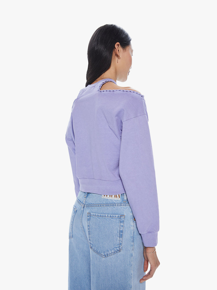 Back view of a woman wearing a cropped lavender pullover featuring dropped sleeves and cut-out shoulders.