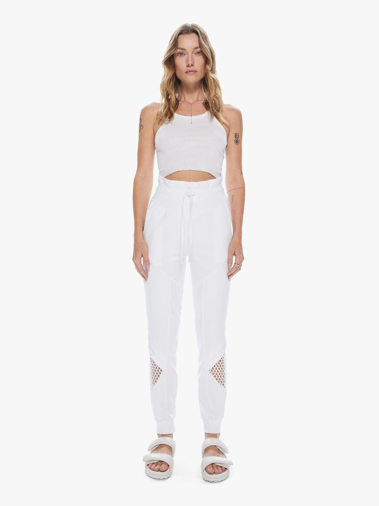 Front view of a woman wearing a pair of white sweatpants featuring a high elastic waist and mesh cutouts at the calves.
