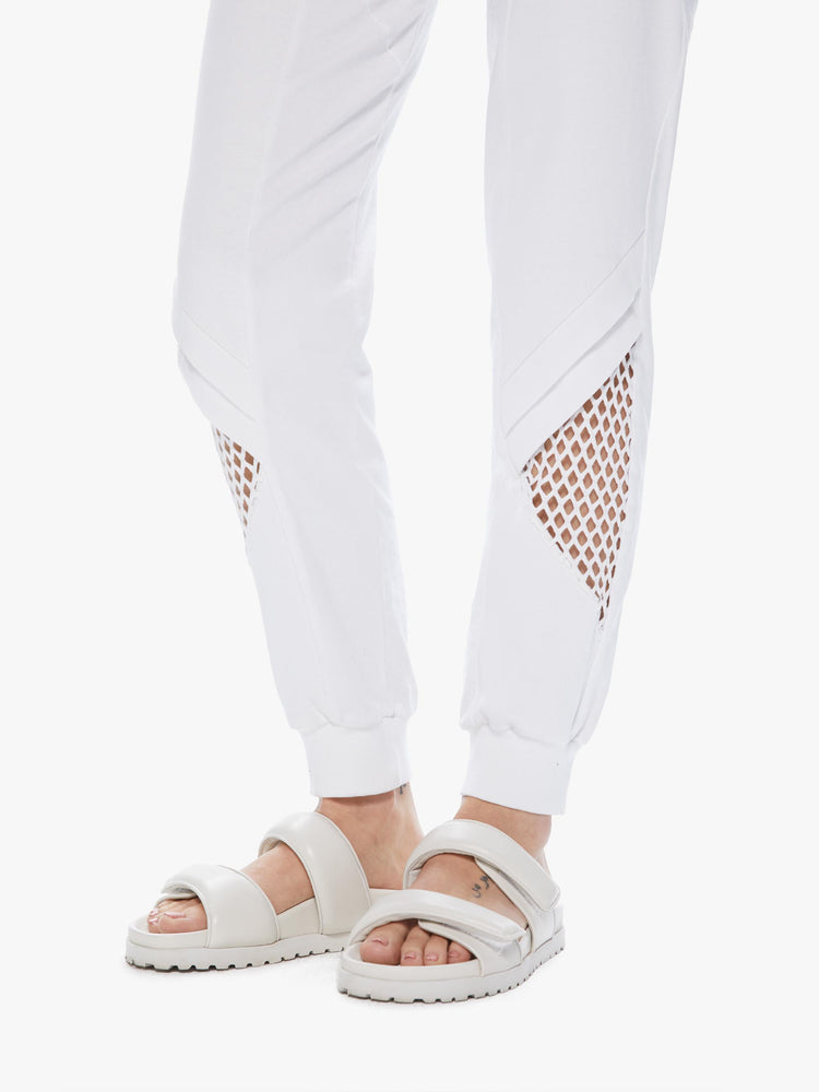 Close up view of a woman wearing a pair of white sweatpants featuring mesh cutouts at the calves.