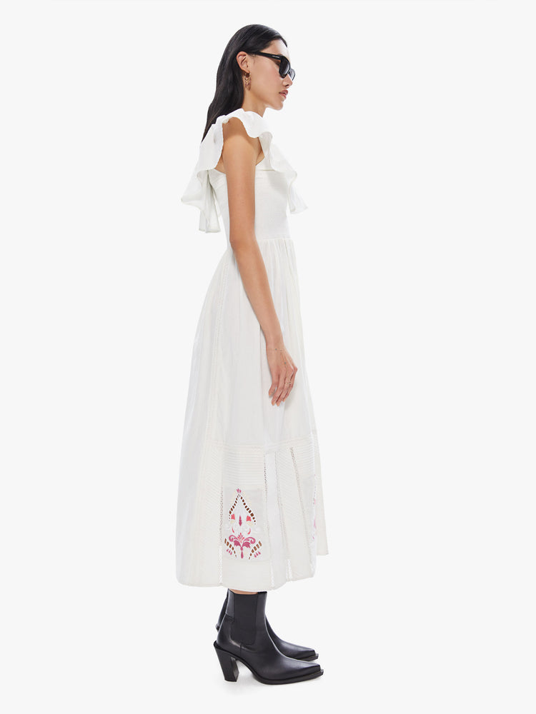 Side view of a women's long white dress with ruffled neckline and sleeves and multi color print at the hem