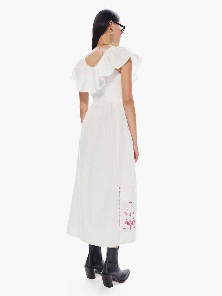 Back view of a women's long white dress with ruffled neckline and sleeves and multi color print at the hem