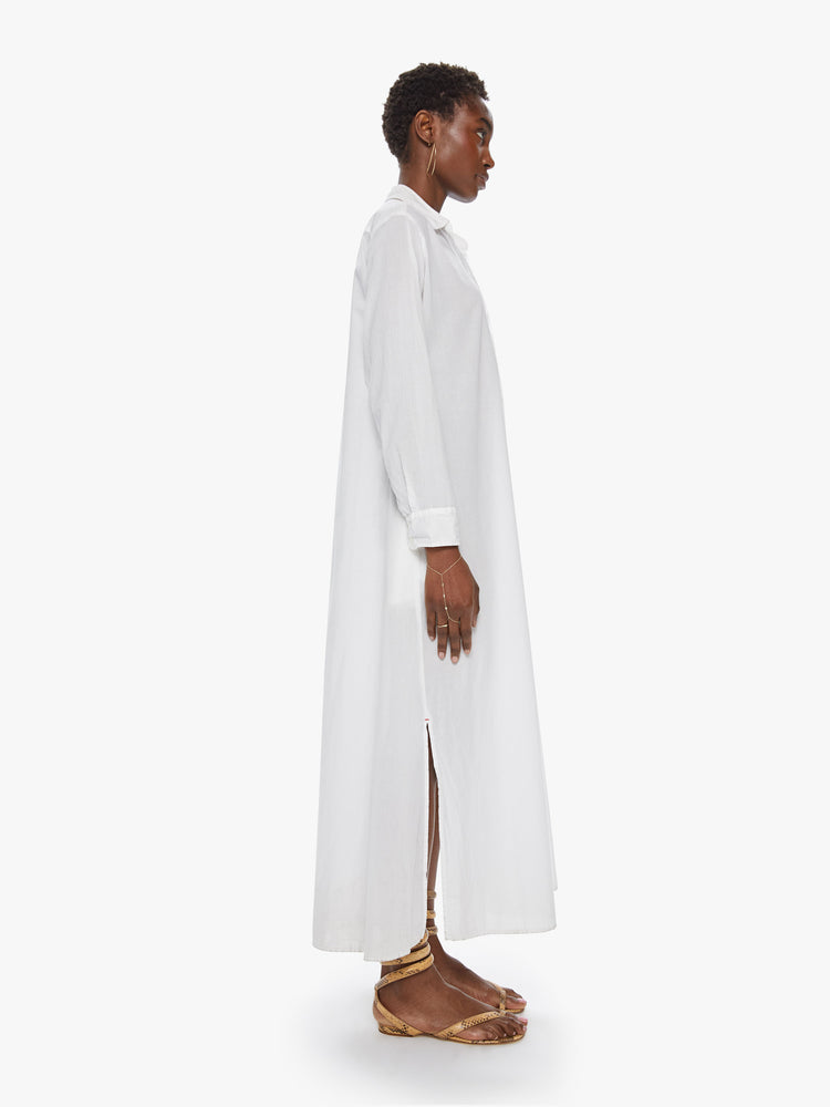 Side view of a women's long white collared shirt dress with long sleeves and side slit
