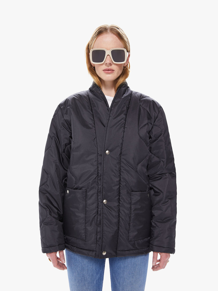 Front view of a women's black quilted jacket, featuring a curved v-neck and front pockets with silver snap buttons and an oversized fit.