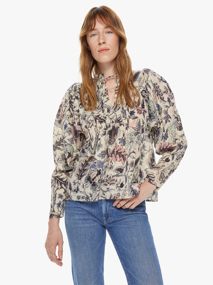 Front view of a woman wearing a long sleeve blouse featuring a neutral floral print and a v-neck with a tie.