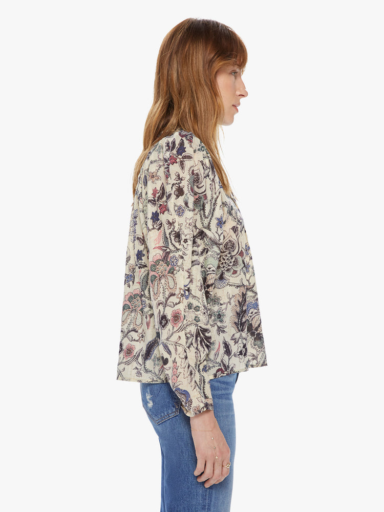 Side view of a woman wearing a long sleeve blouse featuring a neutral floral print and a v-neck with a tie.
