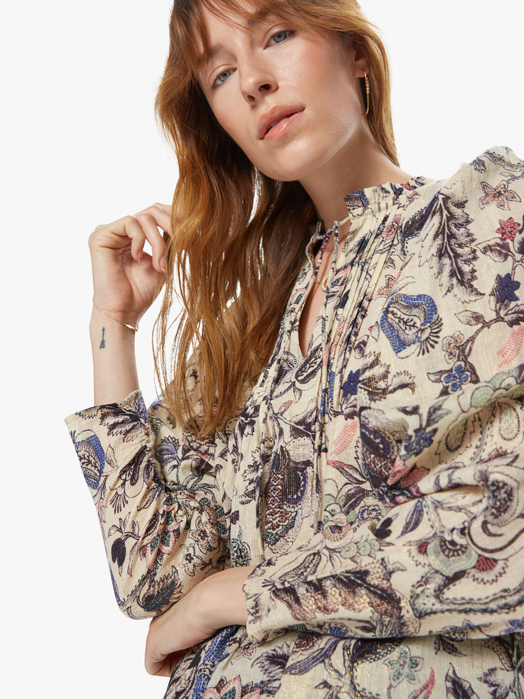 Front close up view of a woman wearing a long sleeve blouse featuring a neutral floral print and a v-neck with a tie.