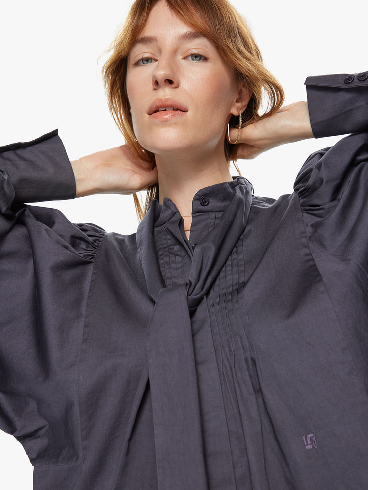 Front close up view of a woman wearing a long sleeve blouse featuring balloon sleeves with a wide cuff, a v-neck button and a neck tie.