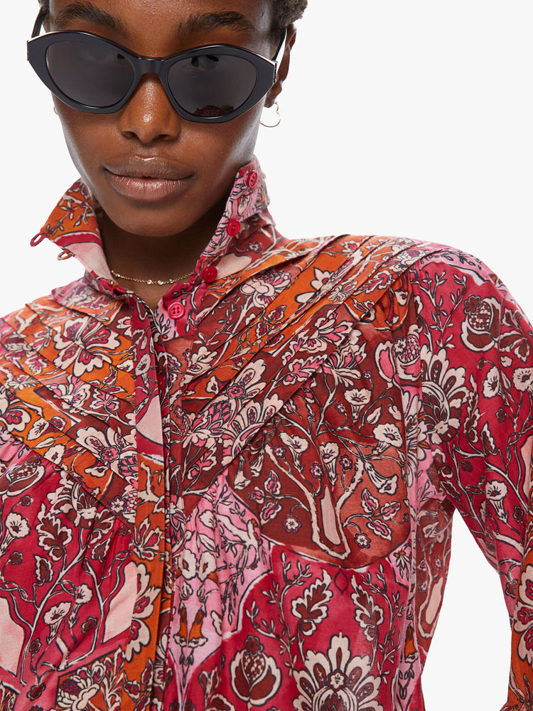 Front close up view of a woman wearing a long sleeve blouse featuring a red and orange floral print, a cropped flowy body, and a high collar.